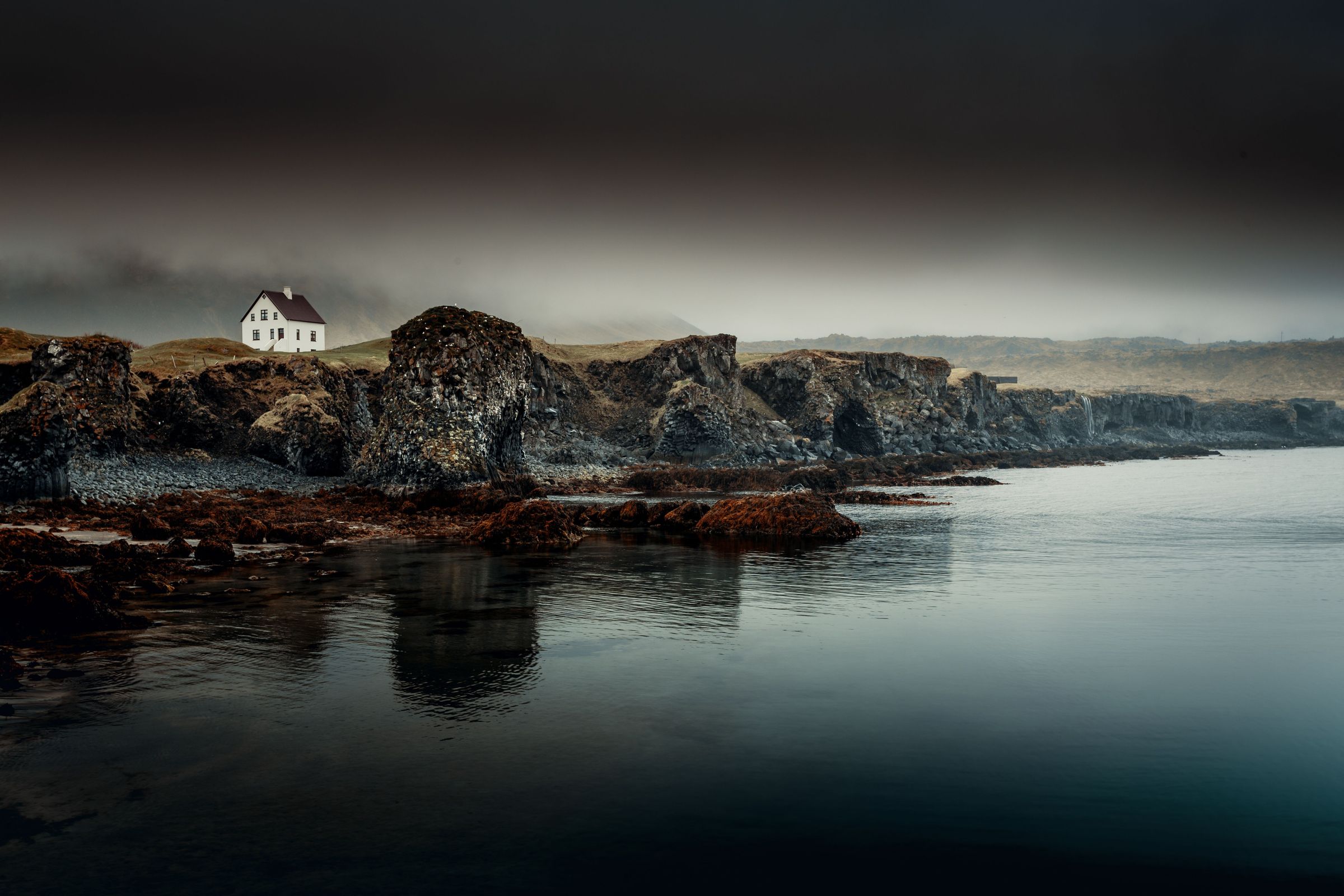 a small white house is sitting on top of a rocky cliff next to a body of water .