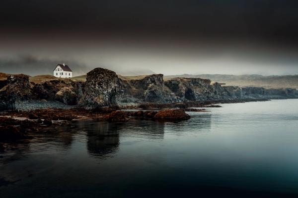 a small white house is sitting on top of a rocky cliff next to a body of water .