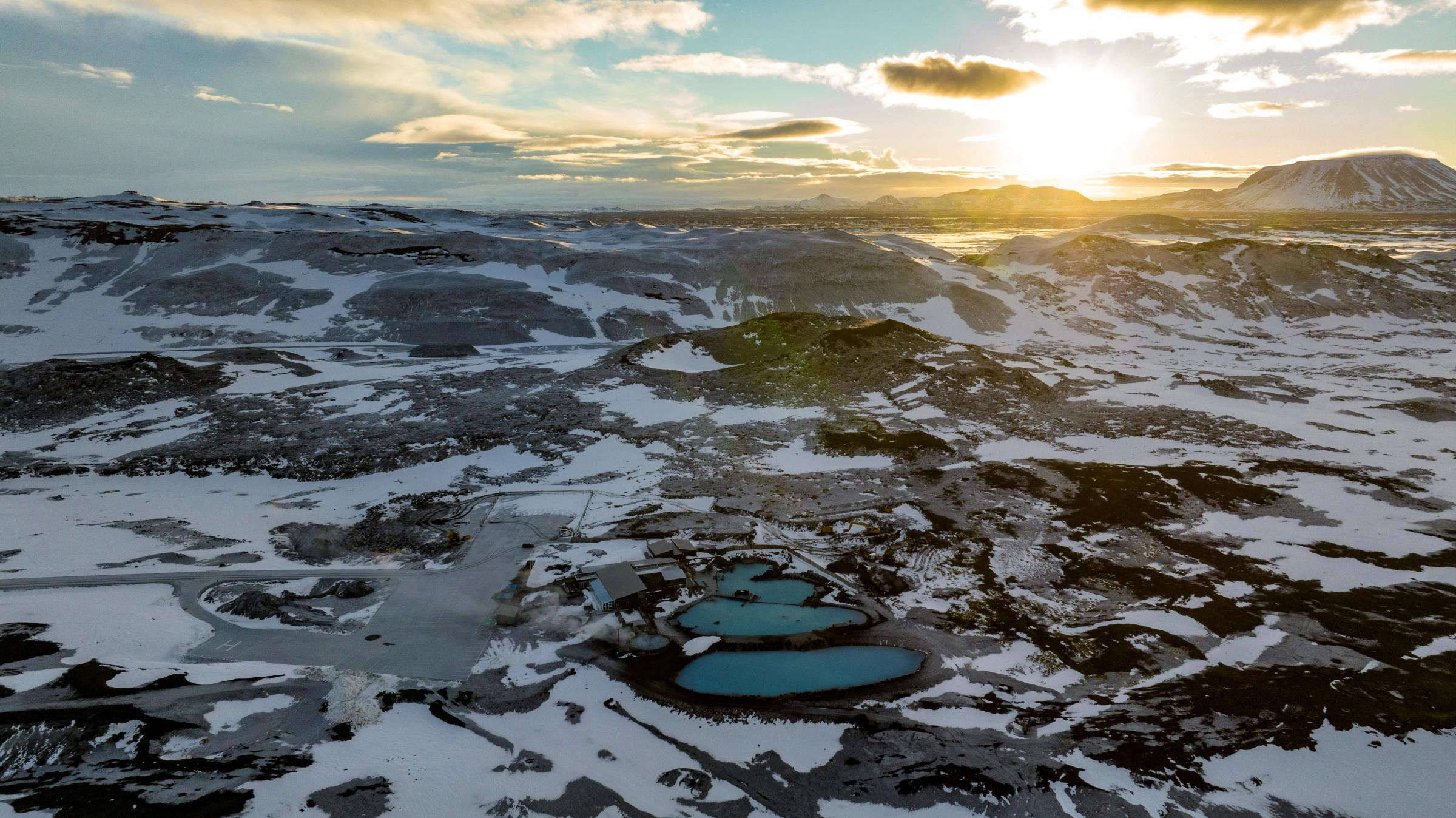una vista aérea de un paisaje nevado con una puesta de sol en el fondo.