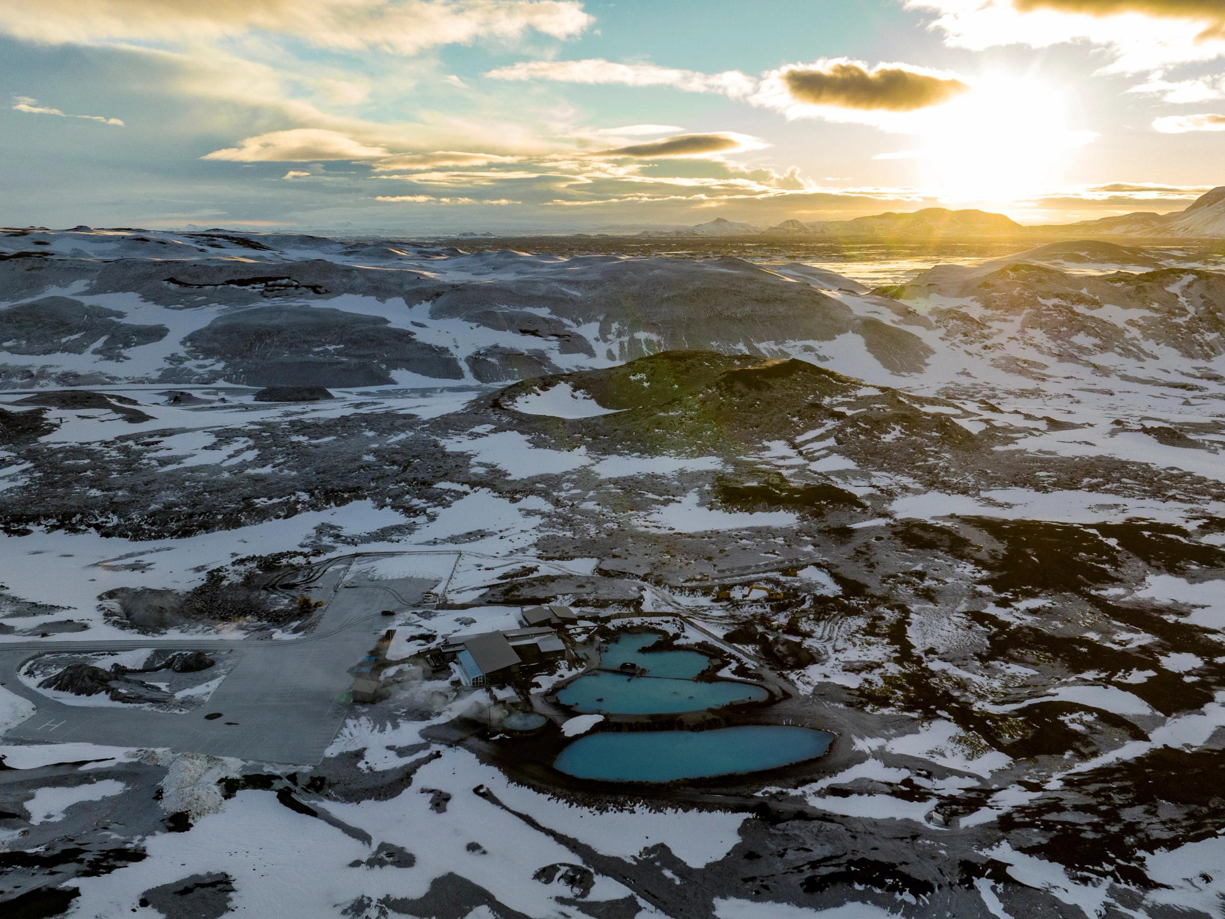 una vista aérea de un paisaje nevado con una puesta de sol en el fondo.
