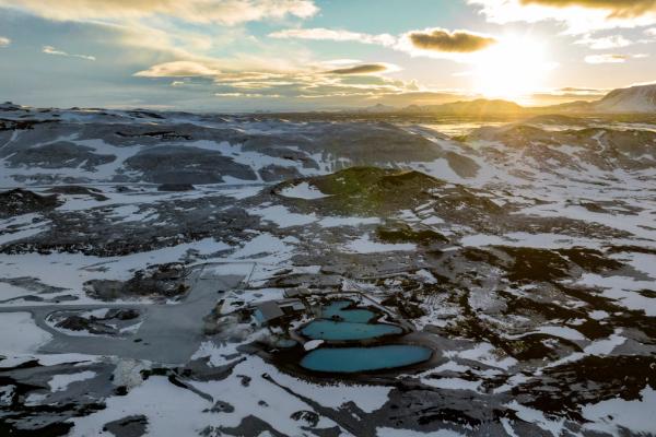Vista aérea de piscinas geotérmicas turquesas en un paisaje volcánico nevado al atardecer.