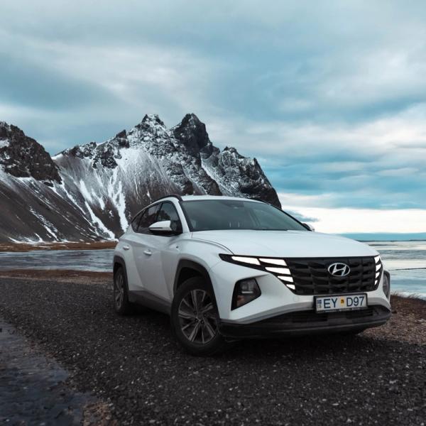 a white hyundai tucson is parked on a gravel road next to a mountain .