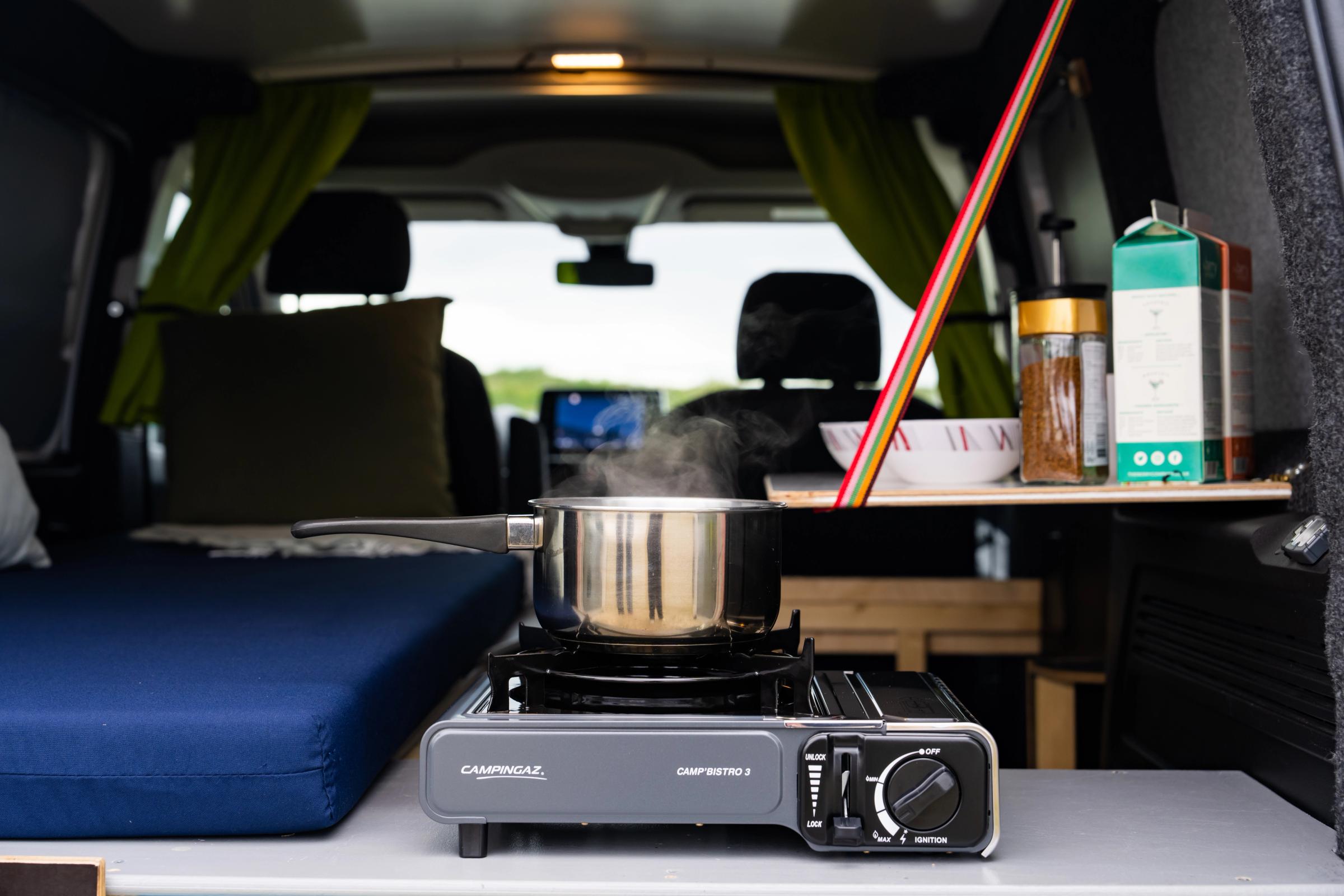 Primer plano de una olla humeante sobre el hornillo de camping, con una mesa, un cuenco y un tarro de café al fondo