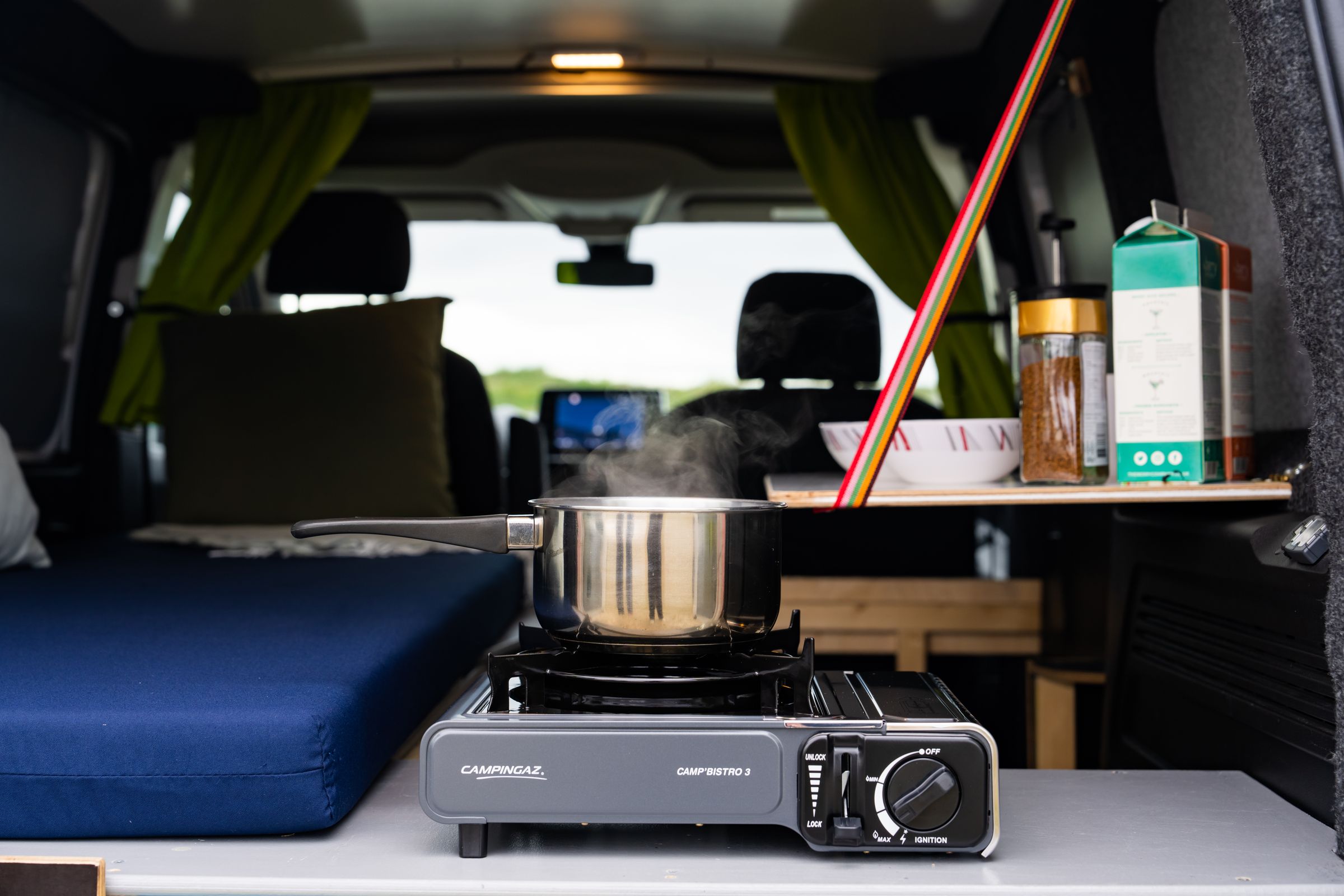 Estufa con olla humeante Primer plano de una olla humeante sobre el hornillo de camping, con una mesa, un cuenco y un tarro de café al fondo