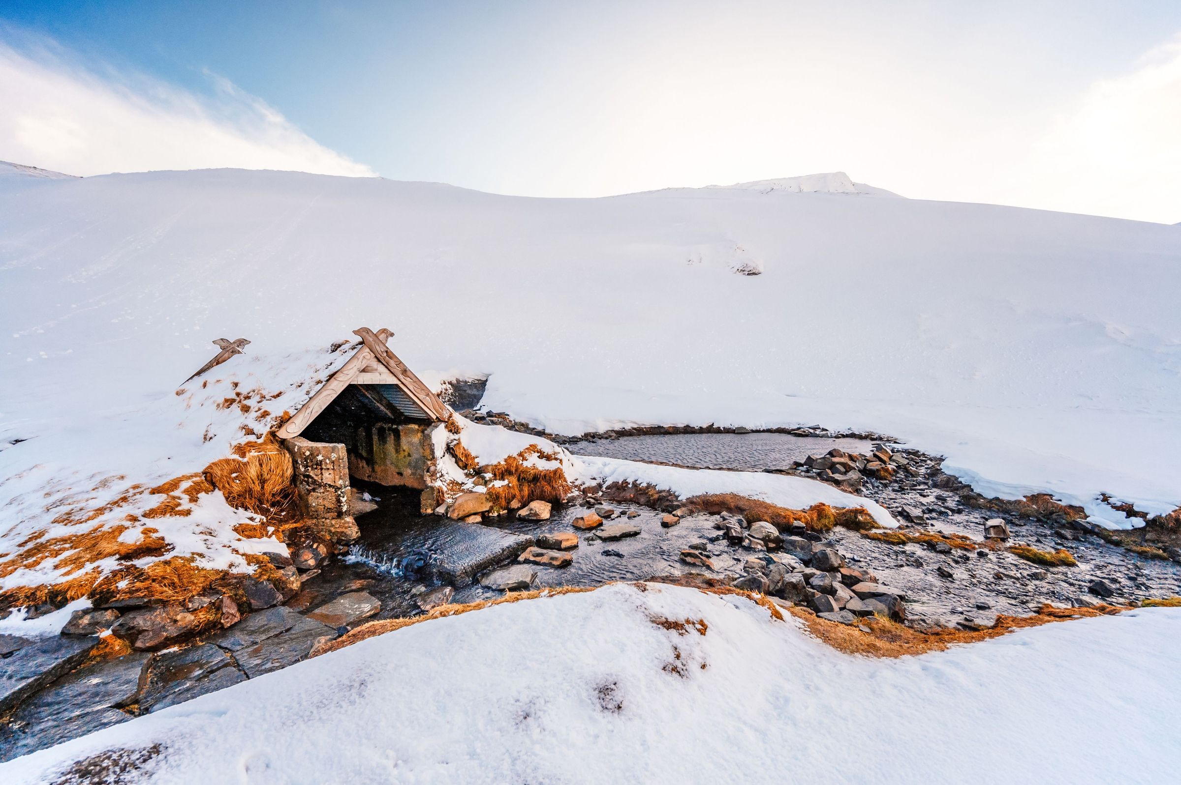 paisaje nevado con unas aguas termales al lado de una pequeña casa de madera