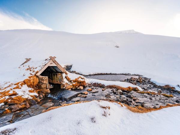 paisaje nevado con unas aguas termales al lado de una pequeña casa de madera