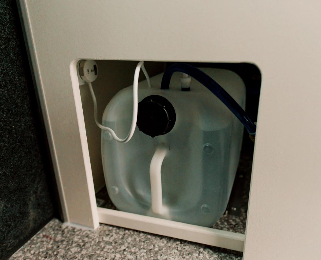 Wasserbehälter mit Schläuchen unter der Spüle in einem großen, günstigen Camper für 5 Personen