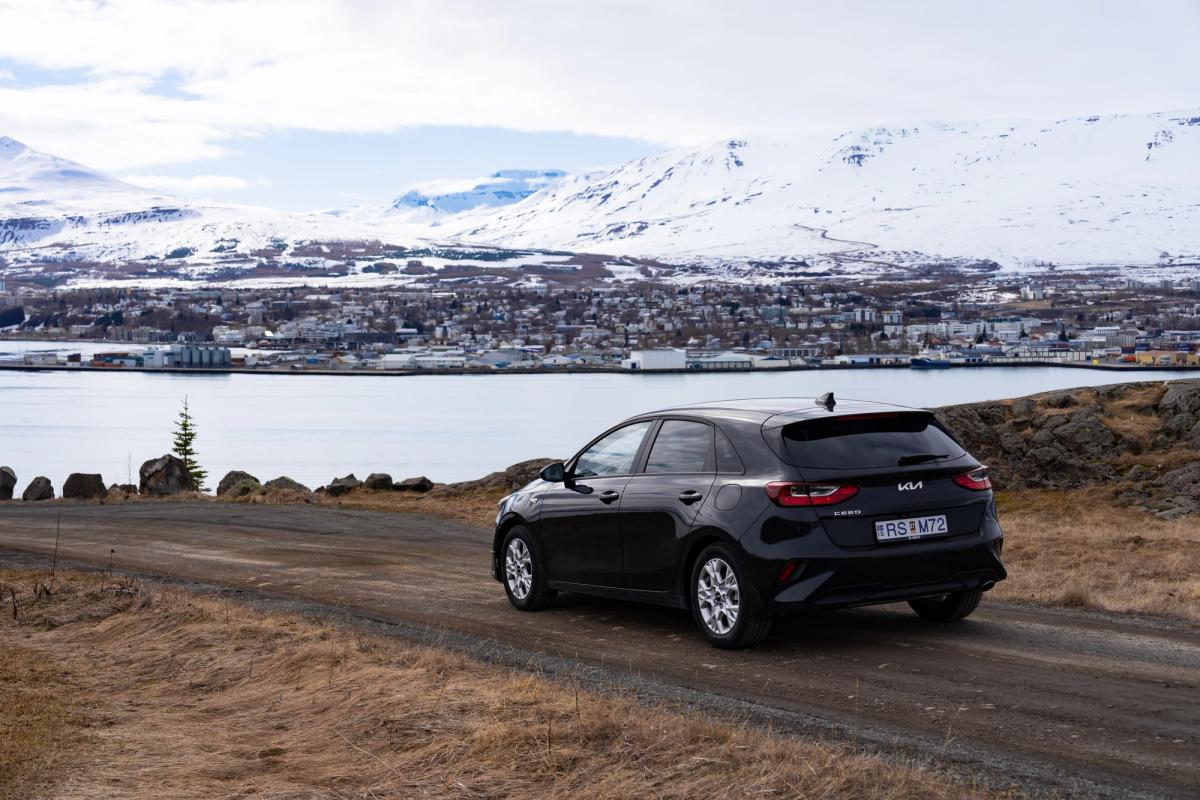 Kia Ceed rear view parked on gravel road above coastal town and mountains