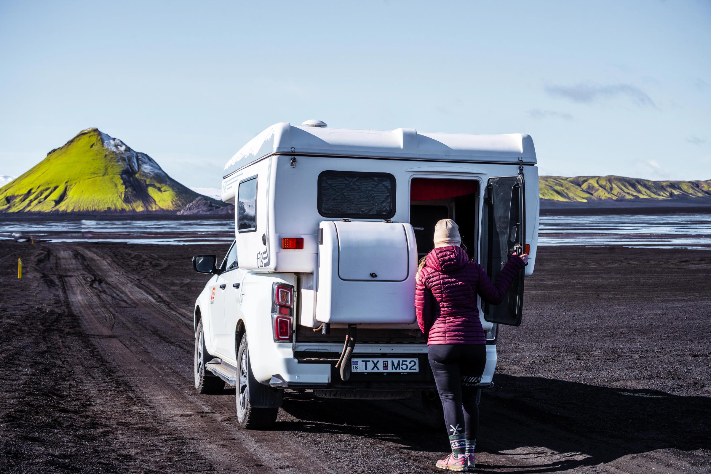 Kona opnar afturhurðina á fjórhjóladrifnum húsbíl á malarvegi, húsbílaleiga á Íslandi