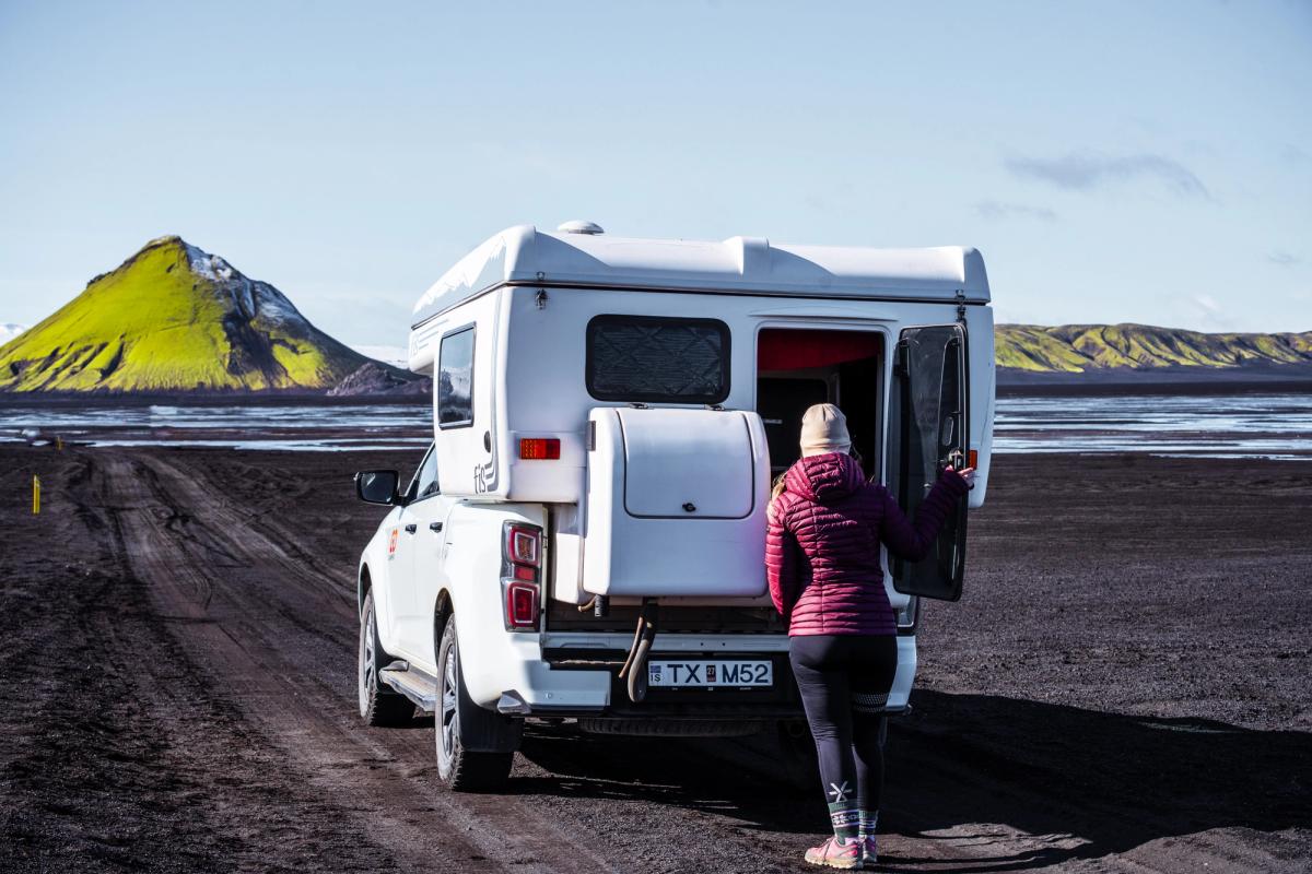 Kona opnar afturhurðina á fjórhjóladrifnum húsbíl á malarvegi, húsbílaleiga á Íslandi