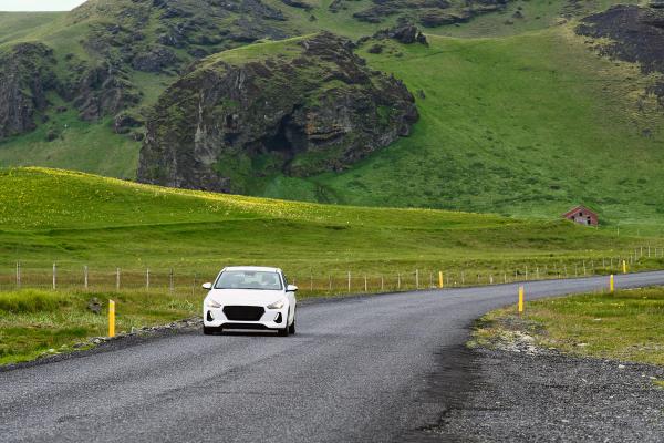 White cars cruising through the vivid summer landscapes of the Icelandic countryside - an idyllic scene of holiday driving adventures. White cars driving on asphalt roads in the green, mountainous Icelandic countryside during summer.