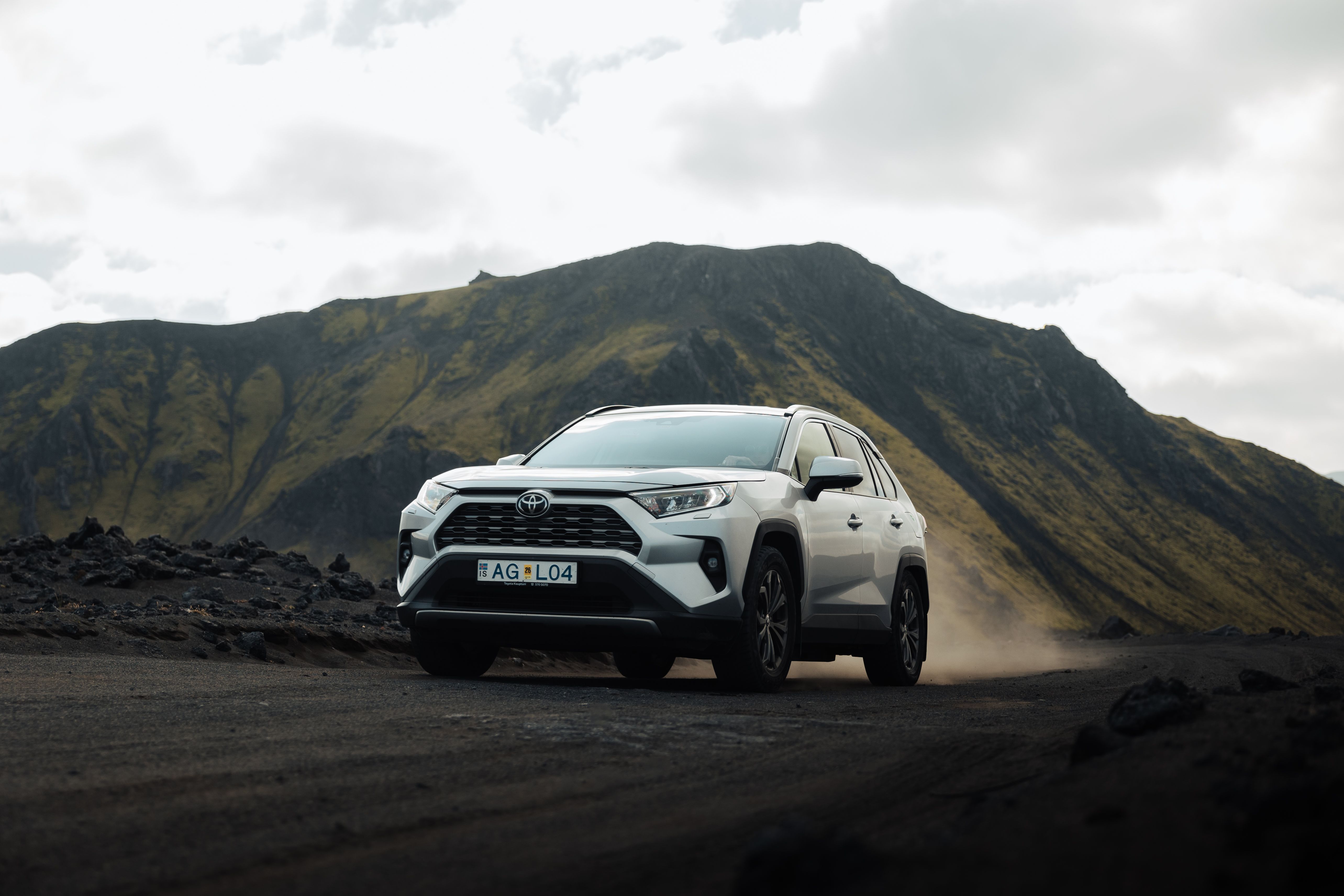 a white toyota rav4 is parked on a dirt road in front of a mountain .