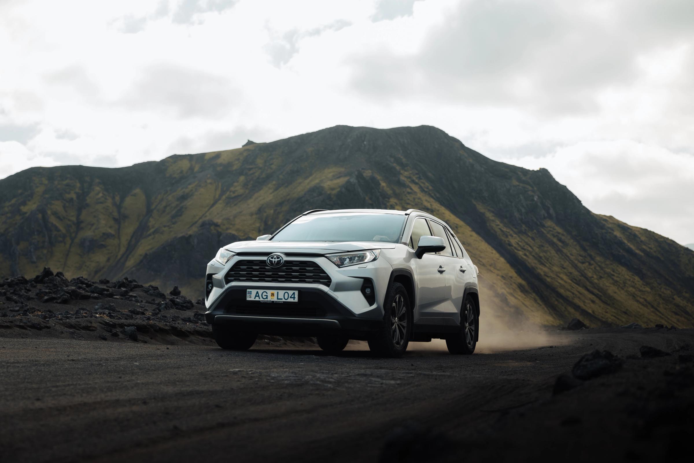 Toyota RAV4 4x4 rental Iceland driving on a gravel road below a mountain slope