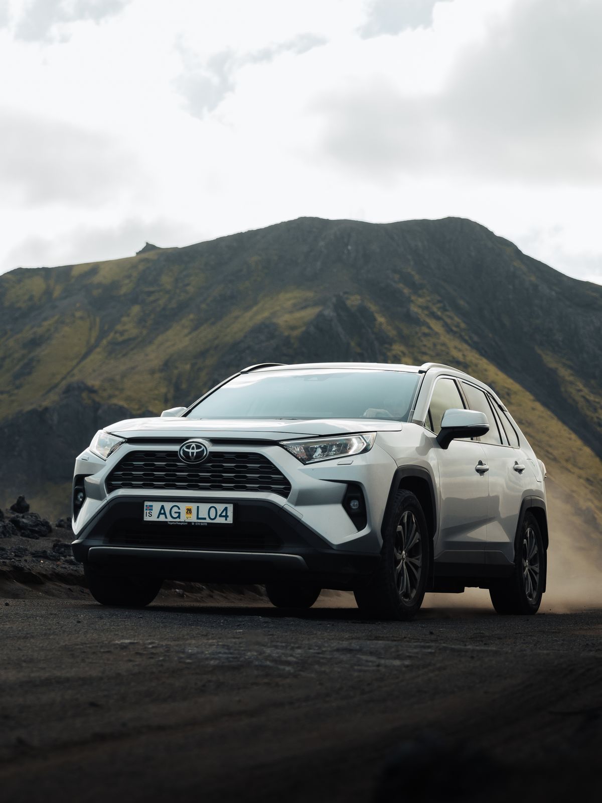a white toyota rav4 is parked on a dirt road in front of a mountain .