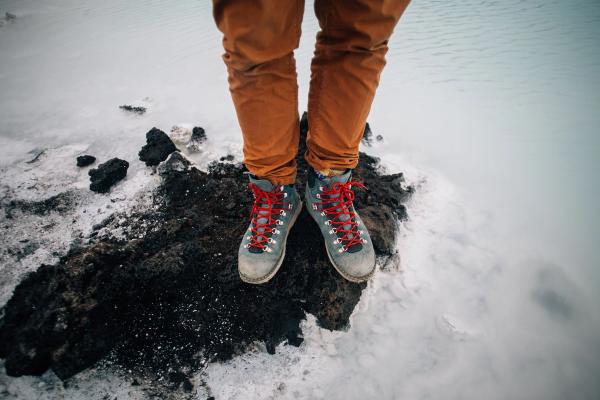 a person wearing hiking boots is standing on a rock in the snow .