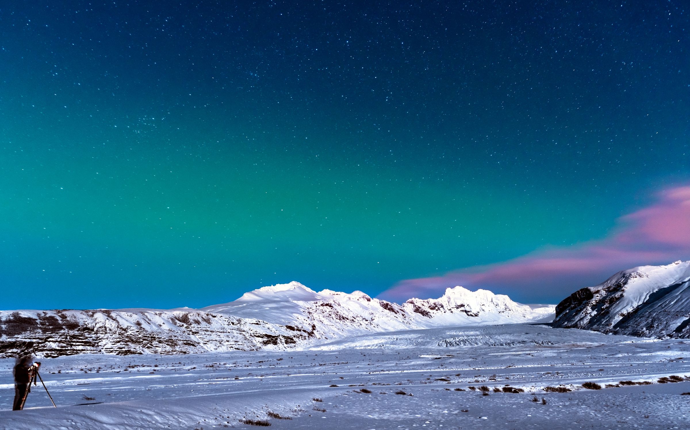 a person is standing in the snow looking at the aurora borealis .