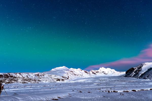a person is standing in the snow looking at the aurora borealis .