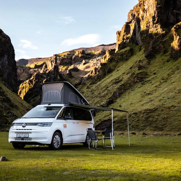 White campervan with the roof-tent open and chairs outside
