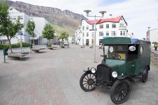 A vintage dark green van parked on a brick-paved street with white buildings and a large mountain in the background.