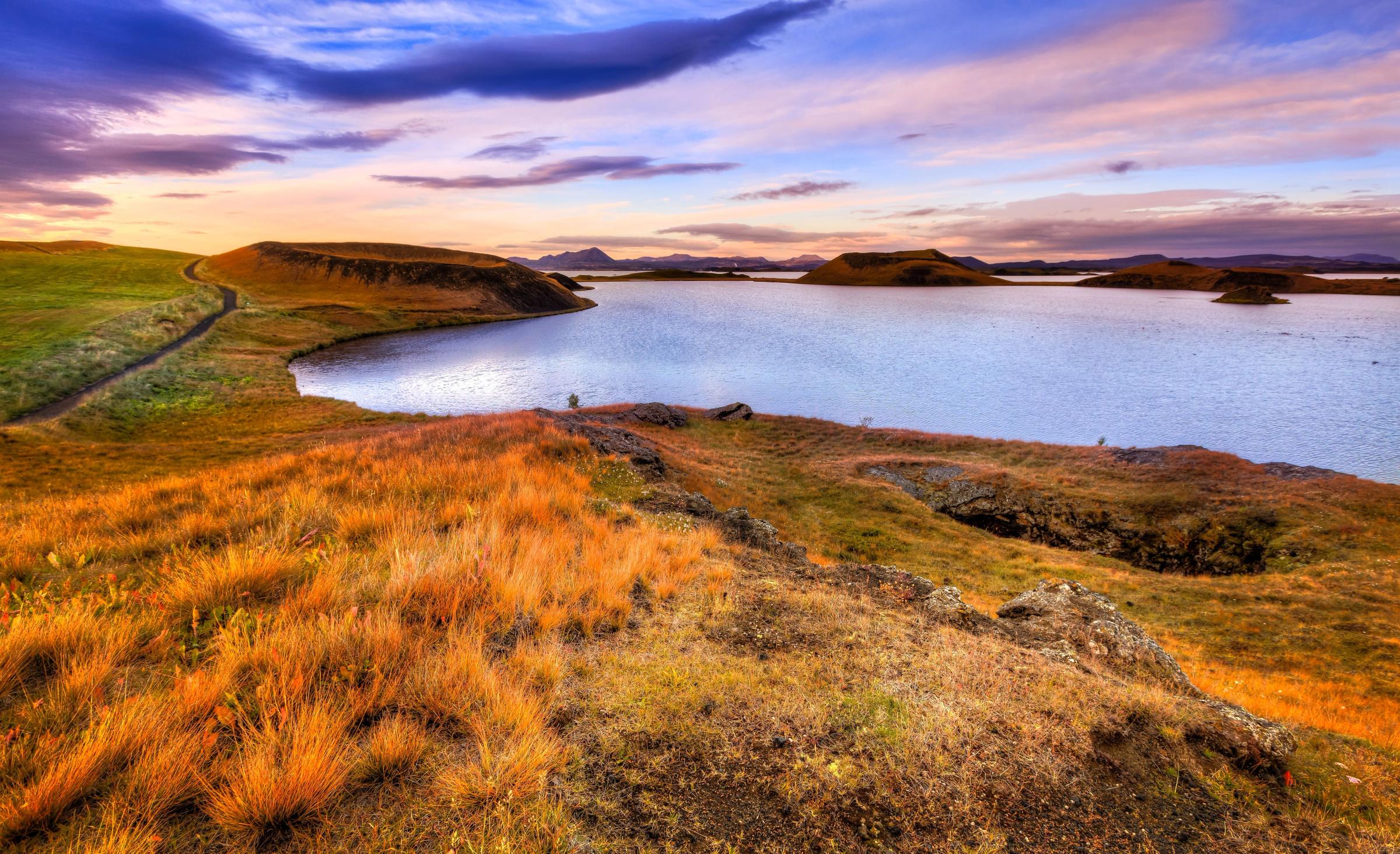 a lake surrounded by grassy hills and mountains at sunset .