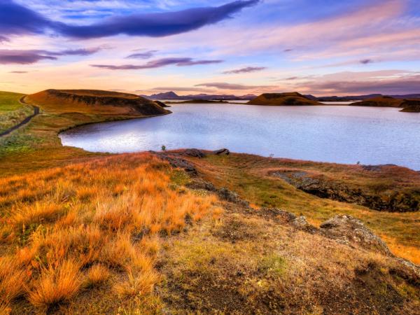 a lake surrounded by grassy hills and mountains at sunset .