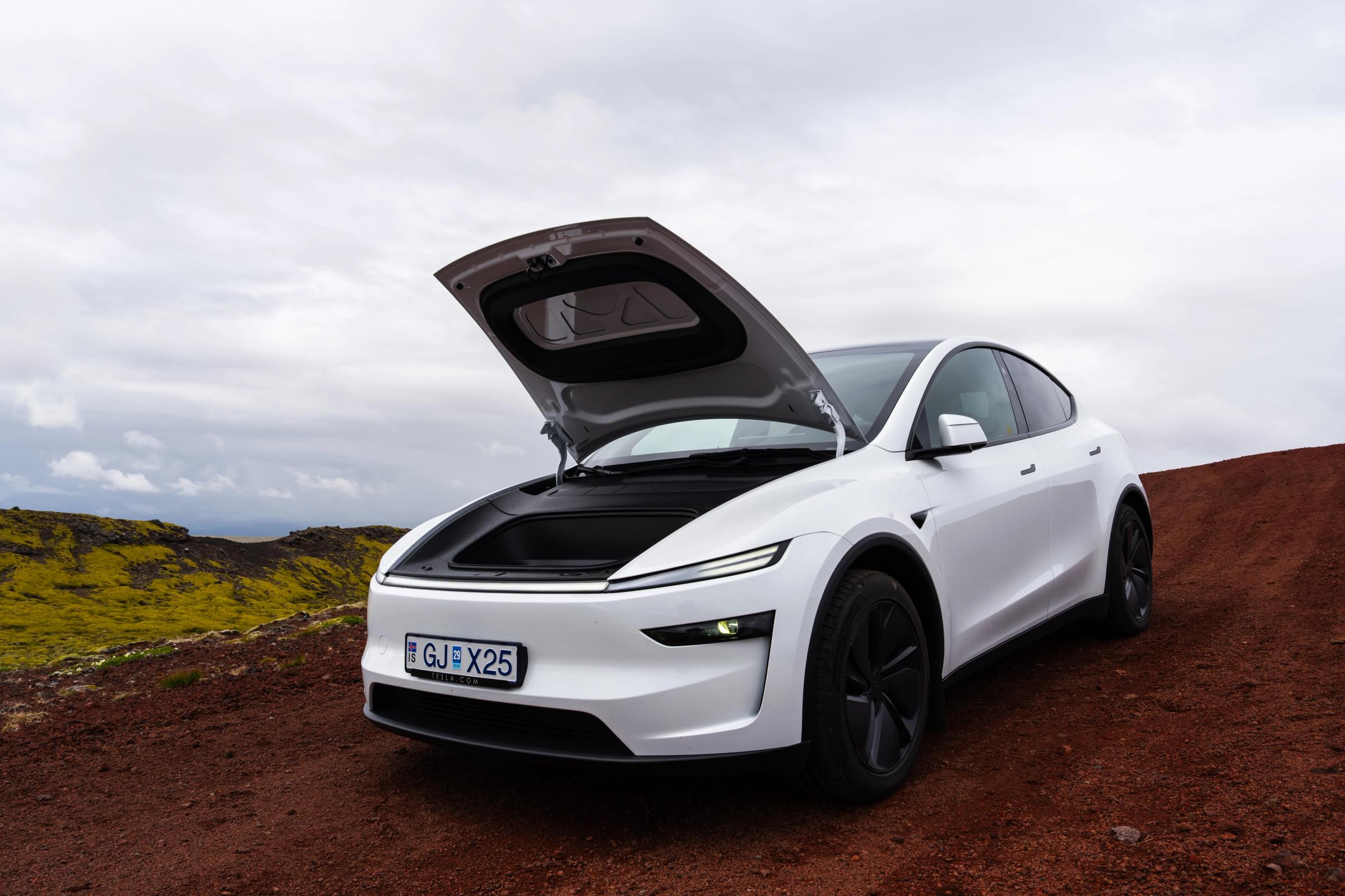 Vista frontal en ángulo del Model Y con el maletero delantero abierto Tesla Model Y 4x4 de alquiler con el maletero delantero abierto, aparcado en un terreno volcánico de Islandia