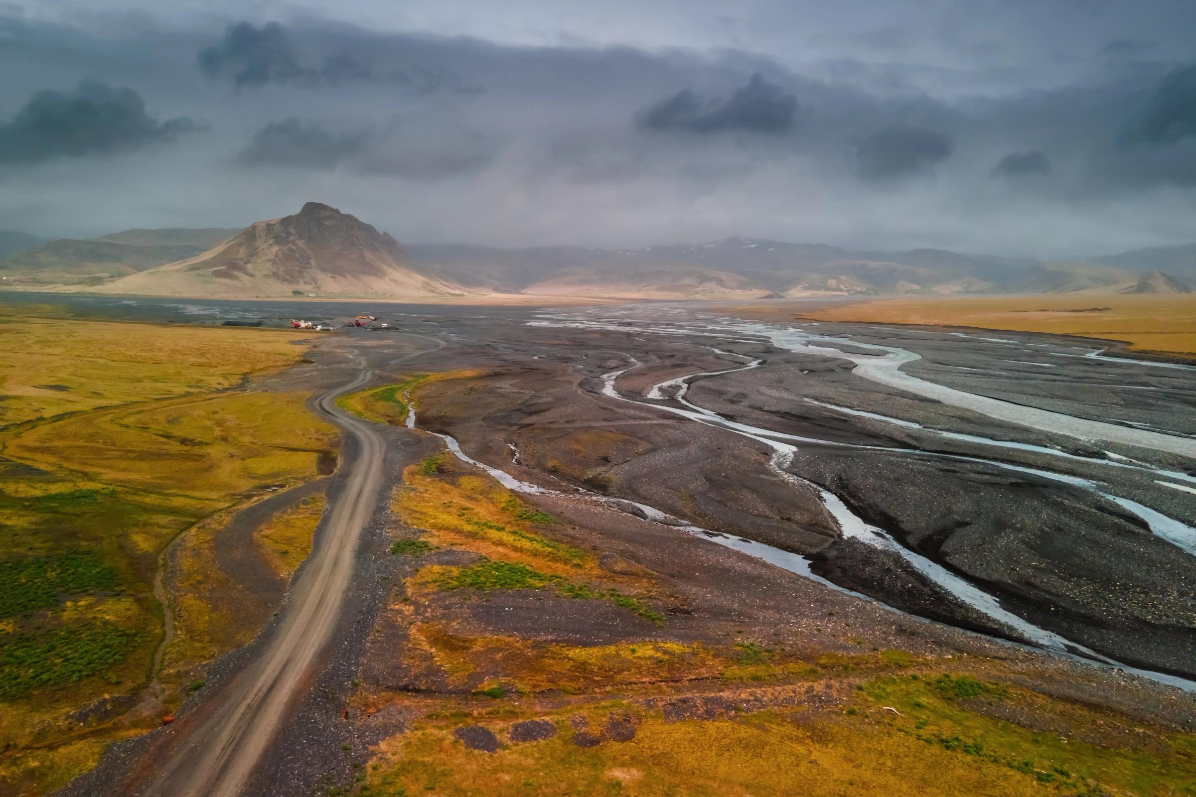 A vast field with a river, a gravel road, and a town and mountains in the background