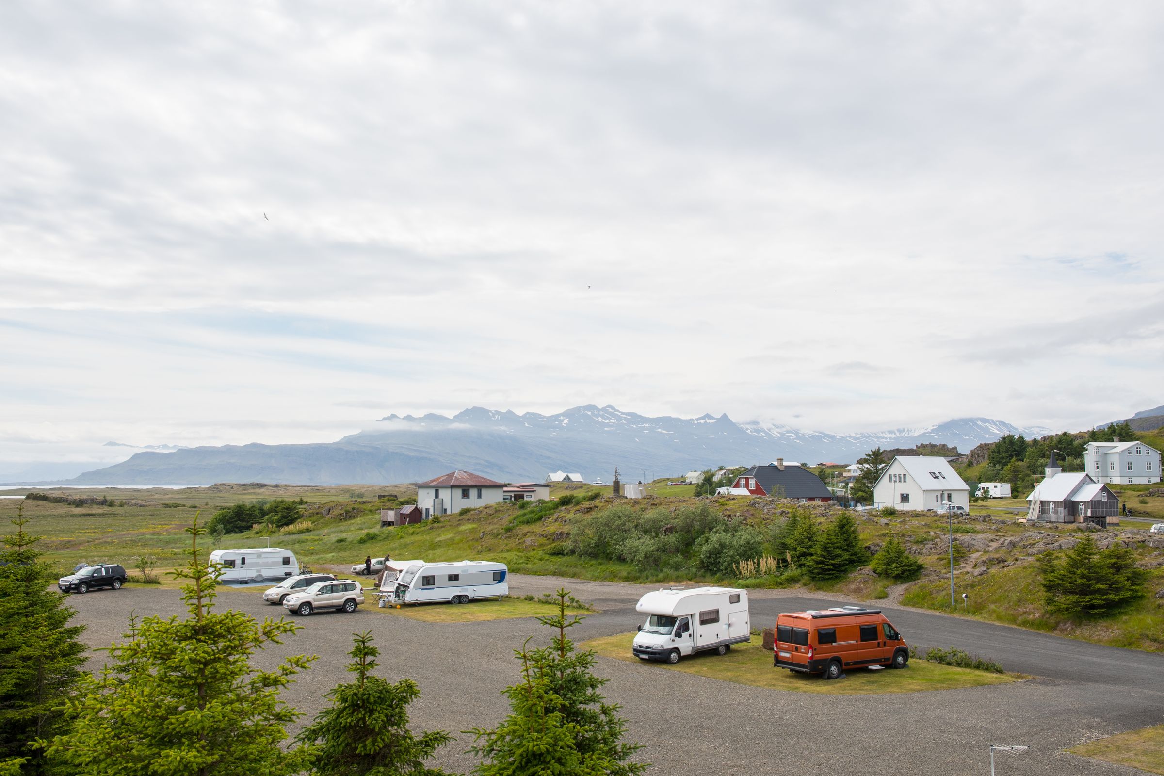 un grupo de casas rodantes están estacionadas en un aparcamiento con montañas de fondo .
