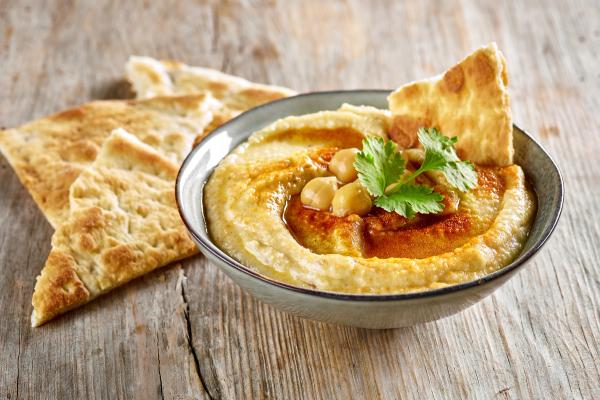 A bowl of hummus garnished with chickpeas, paprika, and cilantro, served with flatbread on a wooden table.