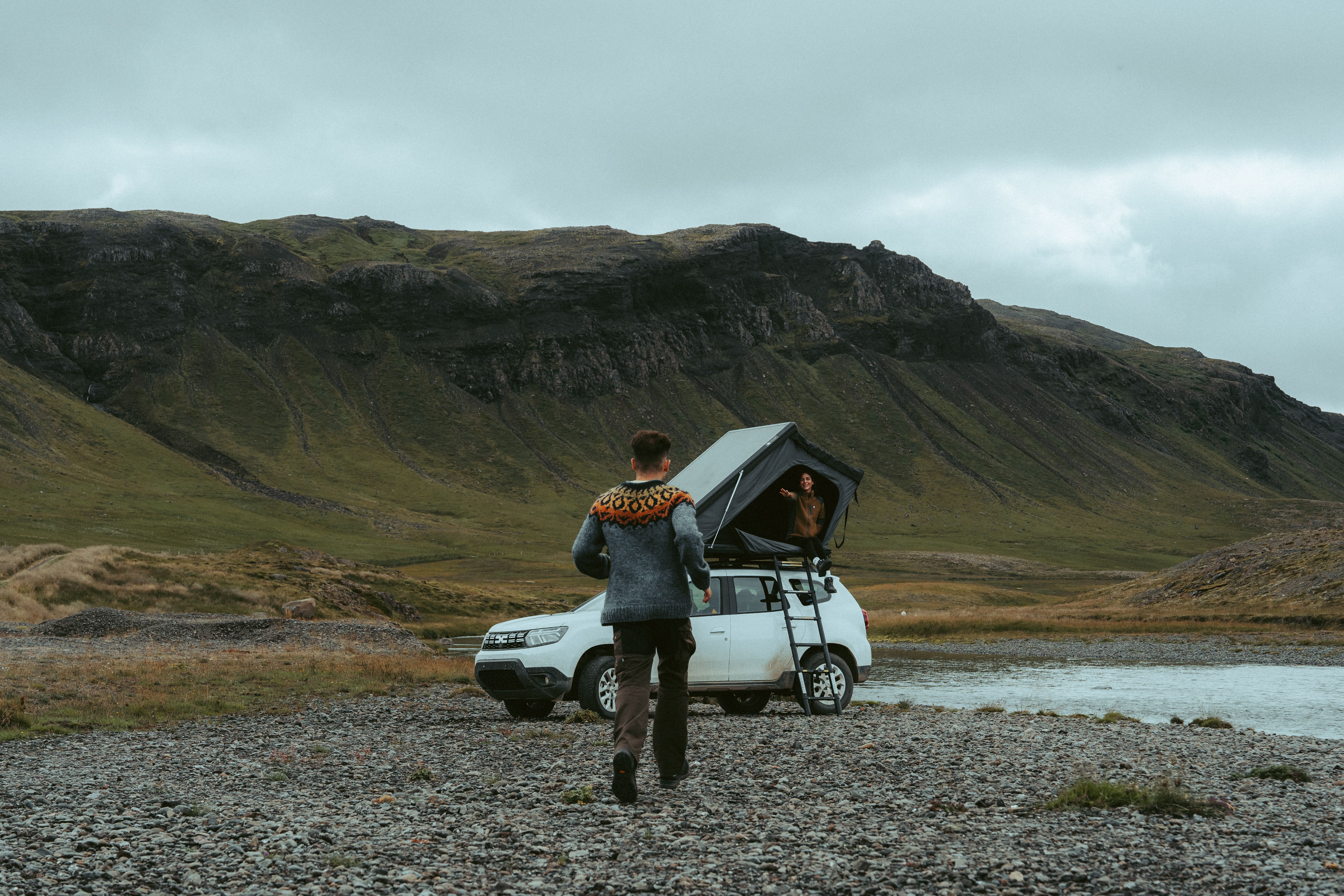 Person walking across a gravel riverbank toward the parked campervan, rooftop tent camper Iceland