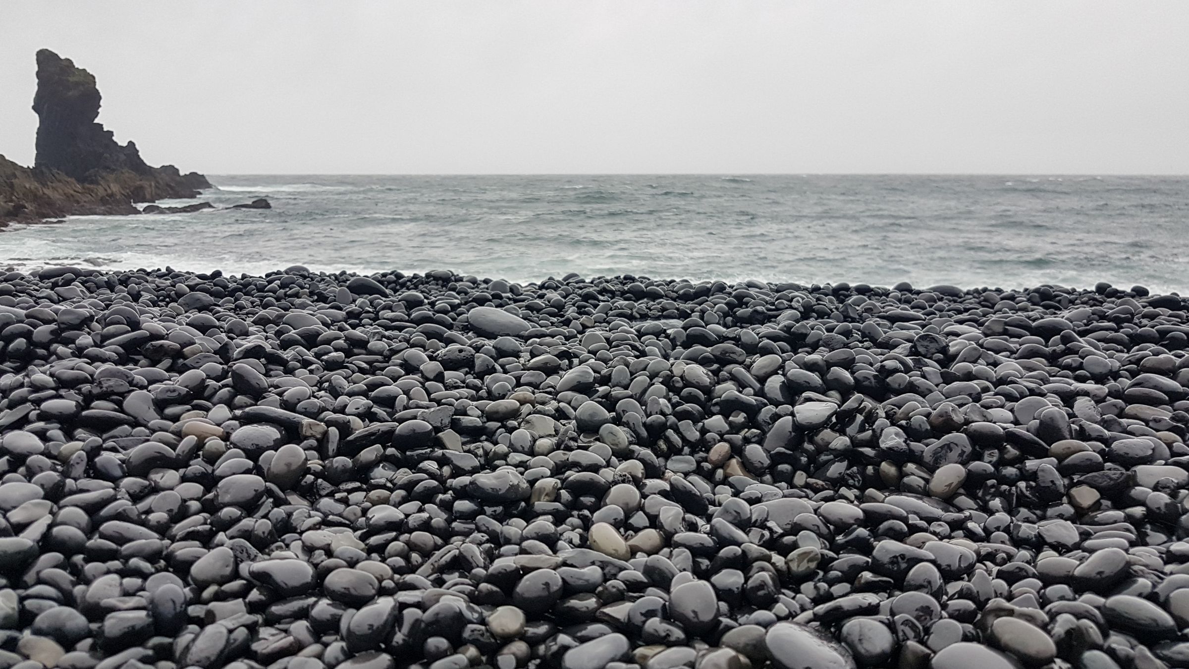 guijarros negros con el mar de fondo