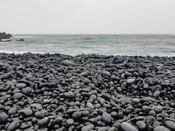 guijarros negros con el mar de fondo