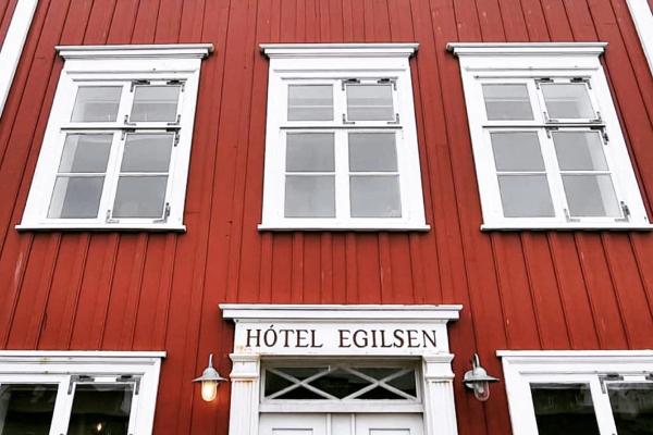the front of a red building with white windows and a sign that says hotel egilsen .