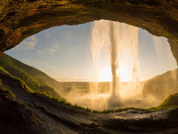 une cascade sort d'une grotte au coucher du soleil.