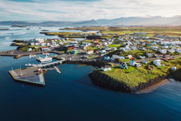 Aerial view of a colorful coastal town with a harbor, boats, green islands, and distant mountains.