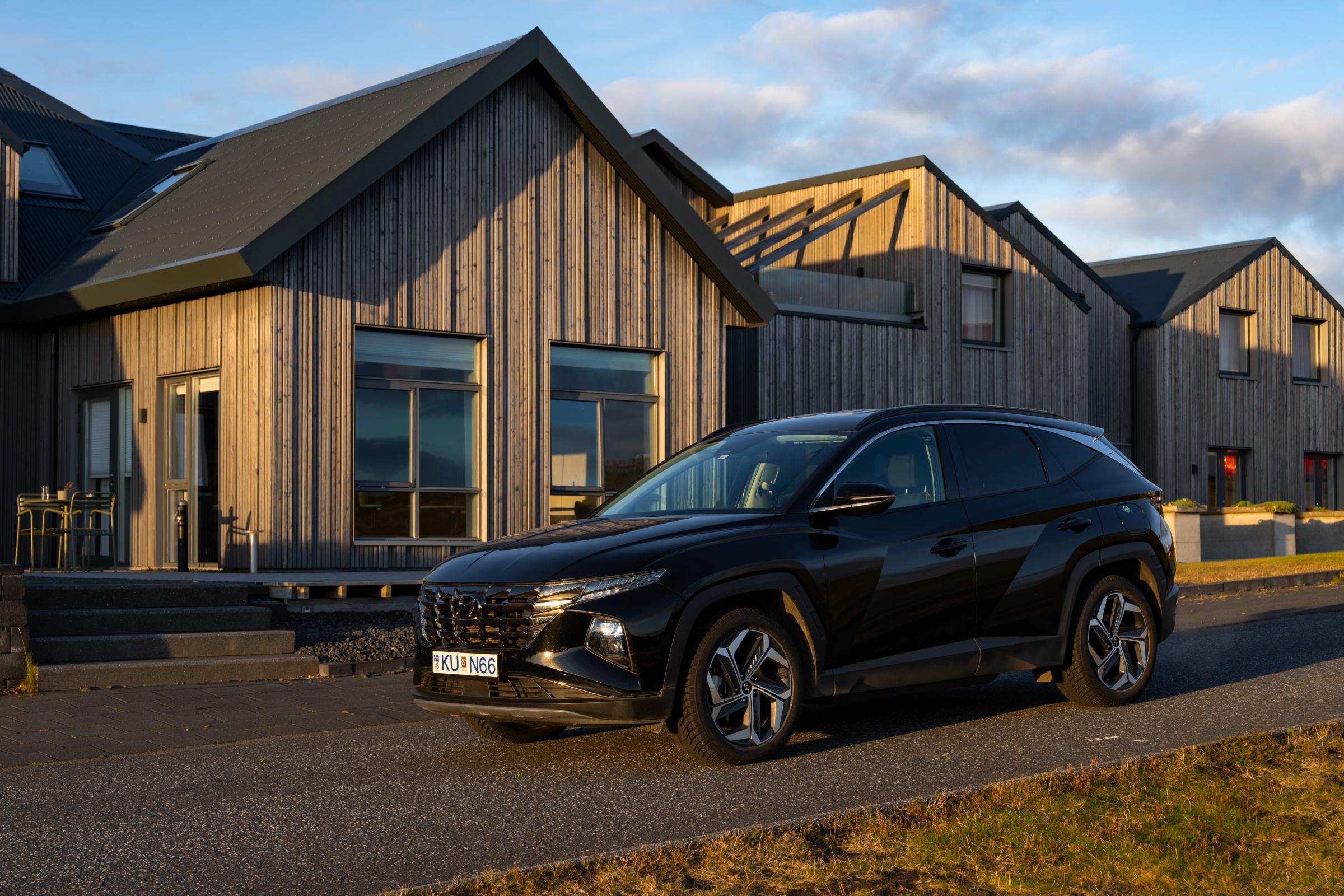 Hyundai Tucson noir vu de trois quarts avant, garé devant une rangée de maisons bardées de bois