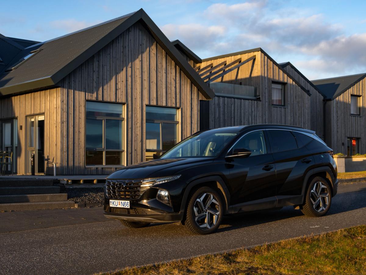 Vue avant trois quarts du Tucson Hyundai Tucson noir vu de trois quarts avant, garé devant une rangée de maisons bardées de bois