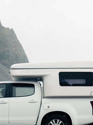 Mujer al lado de una camper blanca en una playa negra