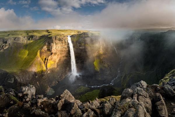 a waterfall is surrounded by rocks and grass in the middle of a canyon .