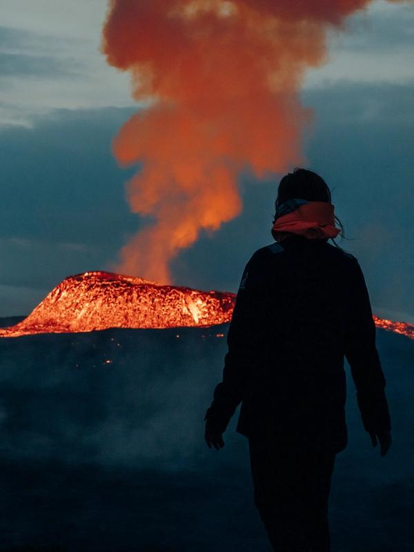 Un hombre de pie frente a un volcán por la noche.