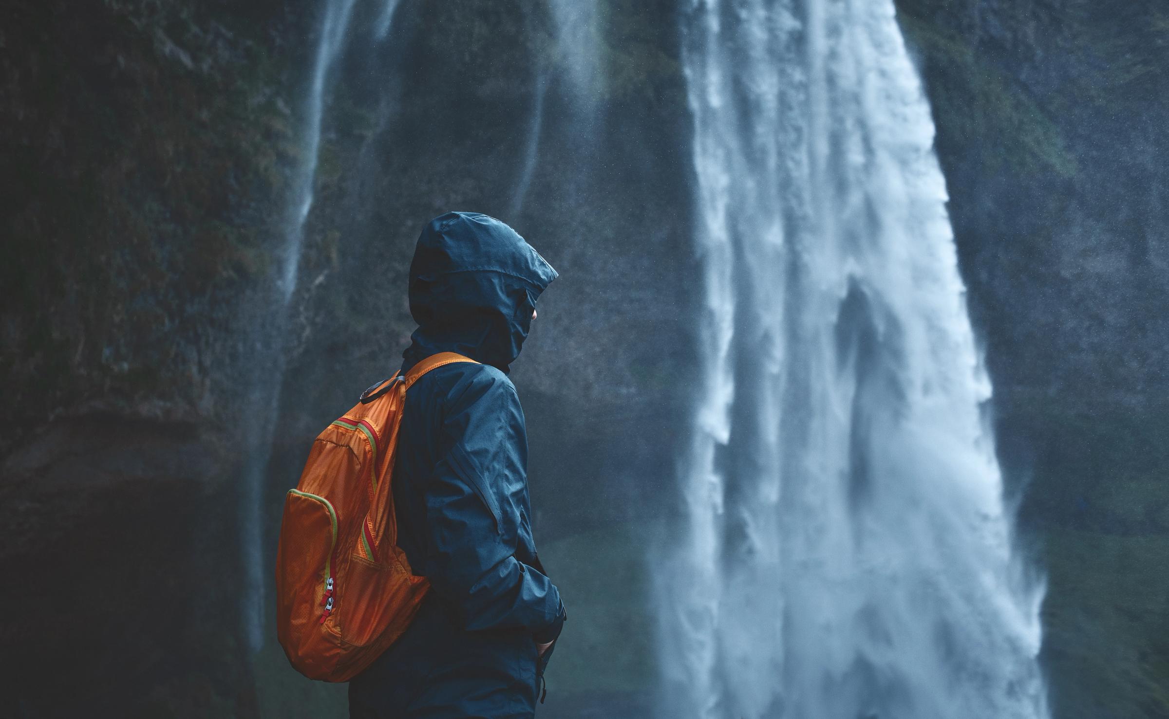 a man standing in front of a waterfall with waterproof jacket and a backpack