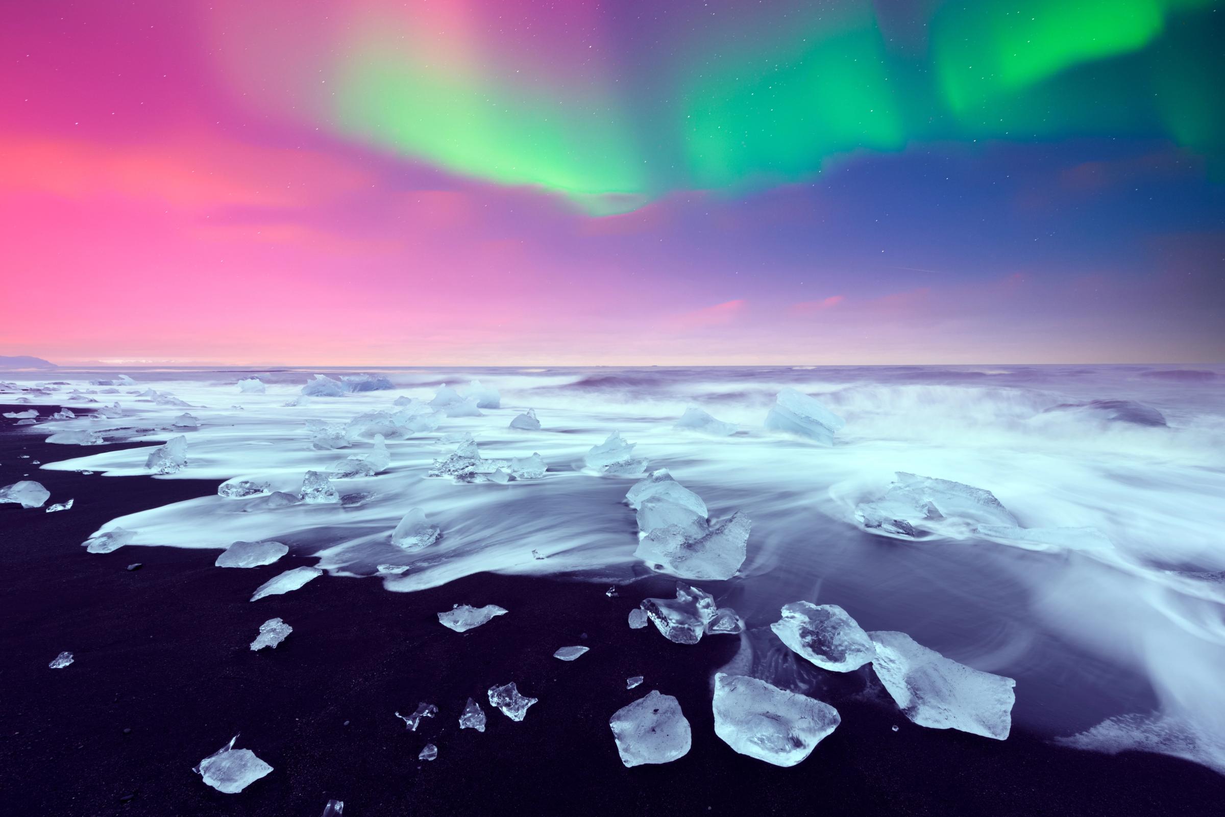 Plage de sable noir avec de petits icebergs et les aurores boréales dans le ciel