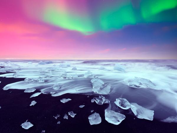 Playa de arena negra con pequeños icebergs y la Aurora Boreal en el cielo