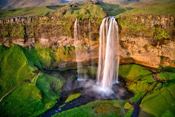an aerial view of a waterfall in the middle of a green field at Seljalandsfoss in iceland.