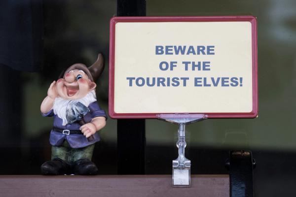 a statue of a gnome holding a sign that says `` beware of the tourist elves '' .