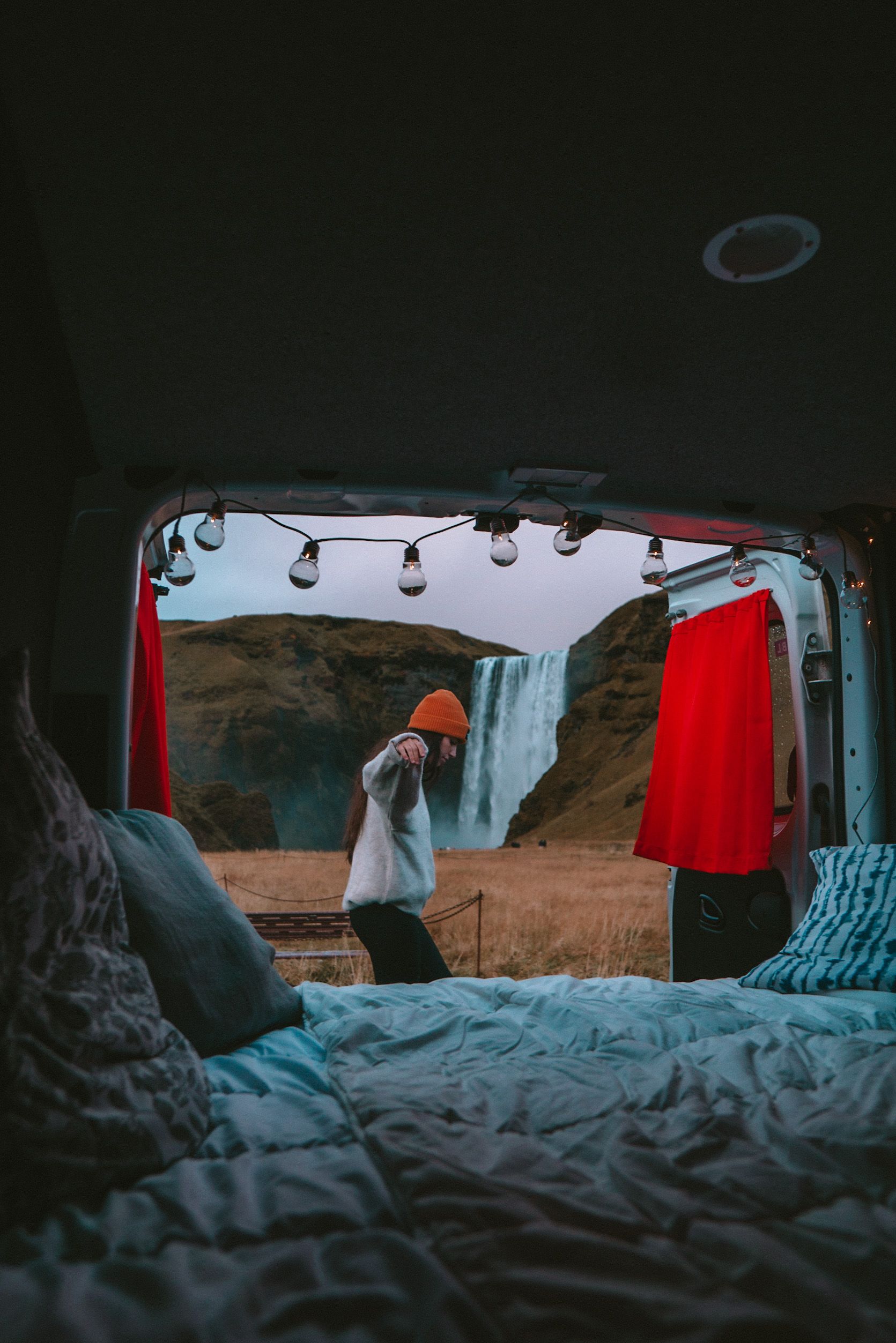 a woman is standing in front of a waterfall in the back of a van