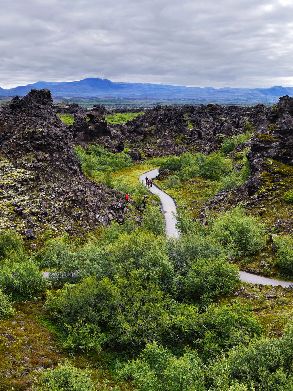 an aerial view of a road surrounded by rocks and trees at Dimmuborgir Lava field in Iceland.