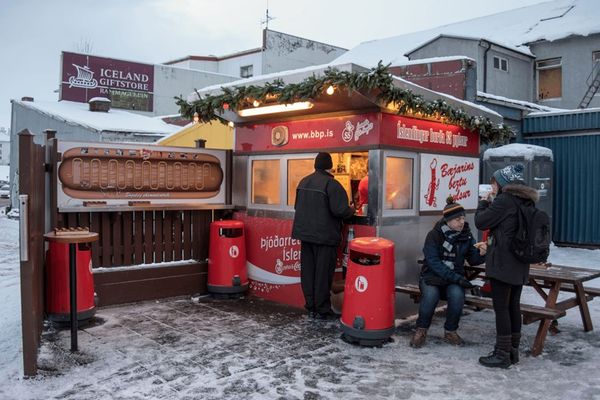 a group of people are standing outside of a hot dog stand in the snow in Reykjavík, iceland.