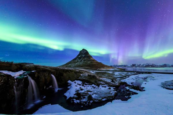 the aurora borealis is shining over a mountain and a waterfall .