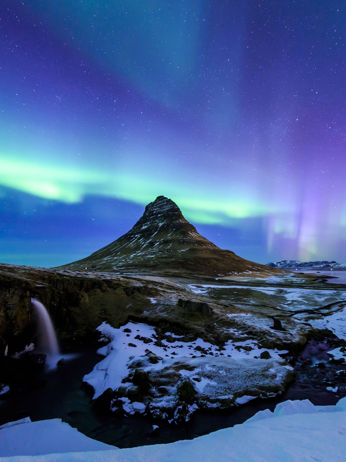 the aurora borealis is shining over a mountain and a waterfall .